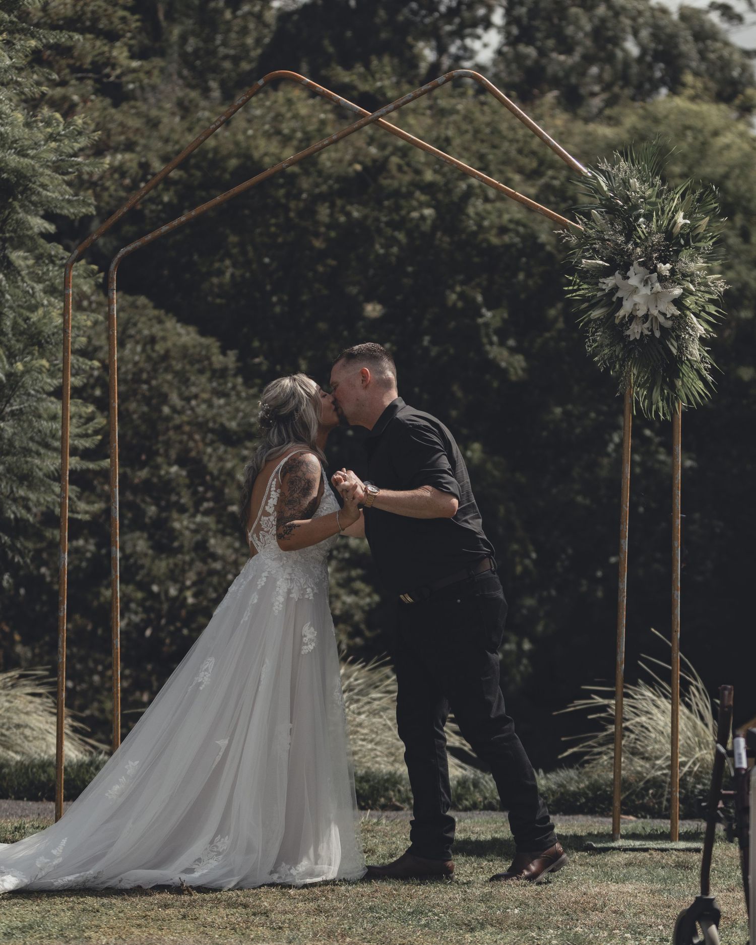 Bride and groom kissing under copper geometric arch at outdoor garden wedding ceremony.