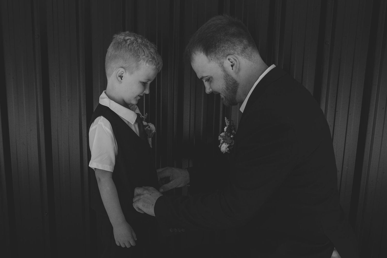 Black and white photo of a groom adjusting a young boy's suit at a wedding ceremony.