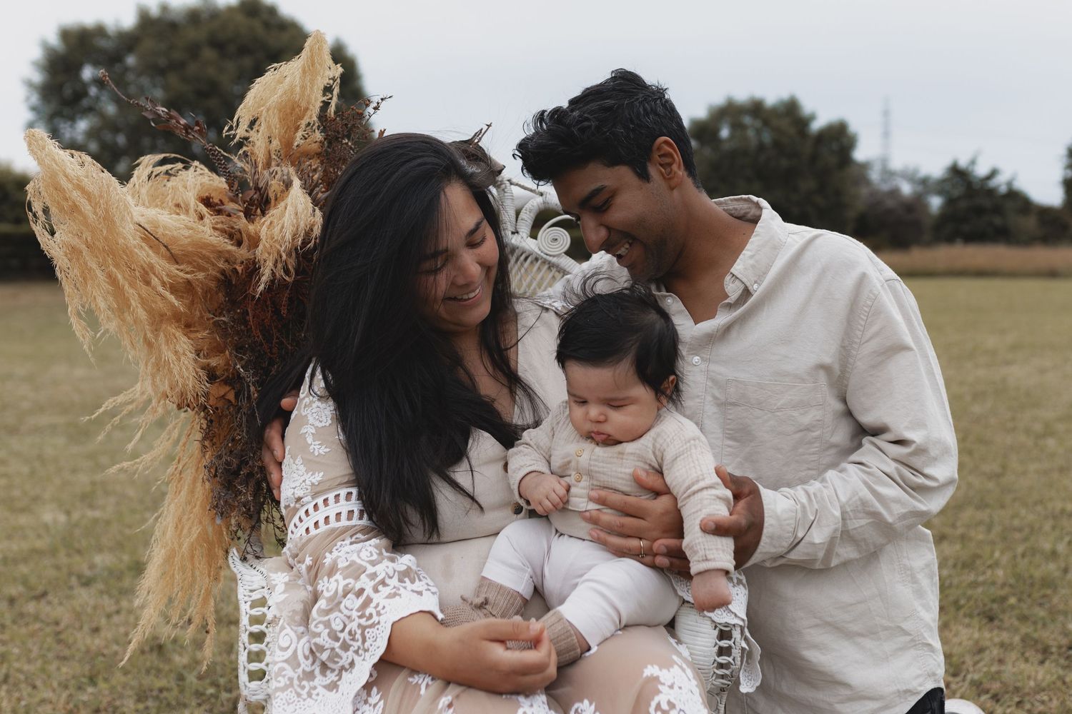 Young family with baby sitting together in open field with pampas grass.