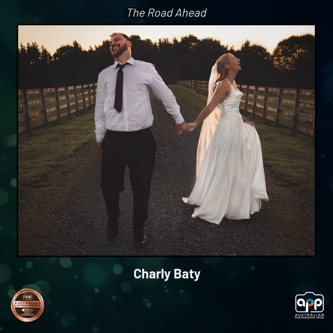Bride and groom walk hand-in-hand down a tree-lined path at sunset in award-winning wedding photo by Charly Baty.