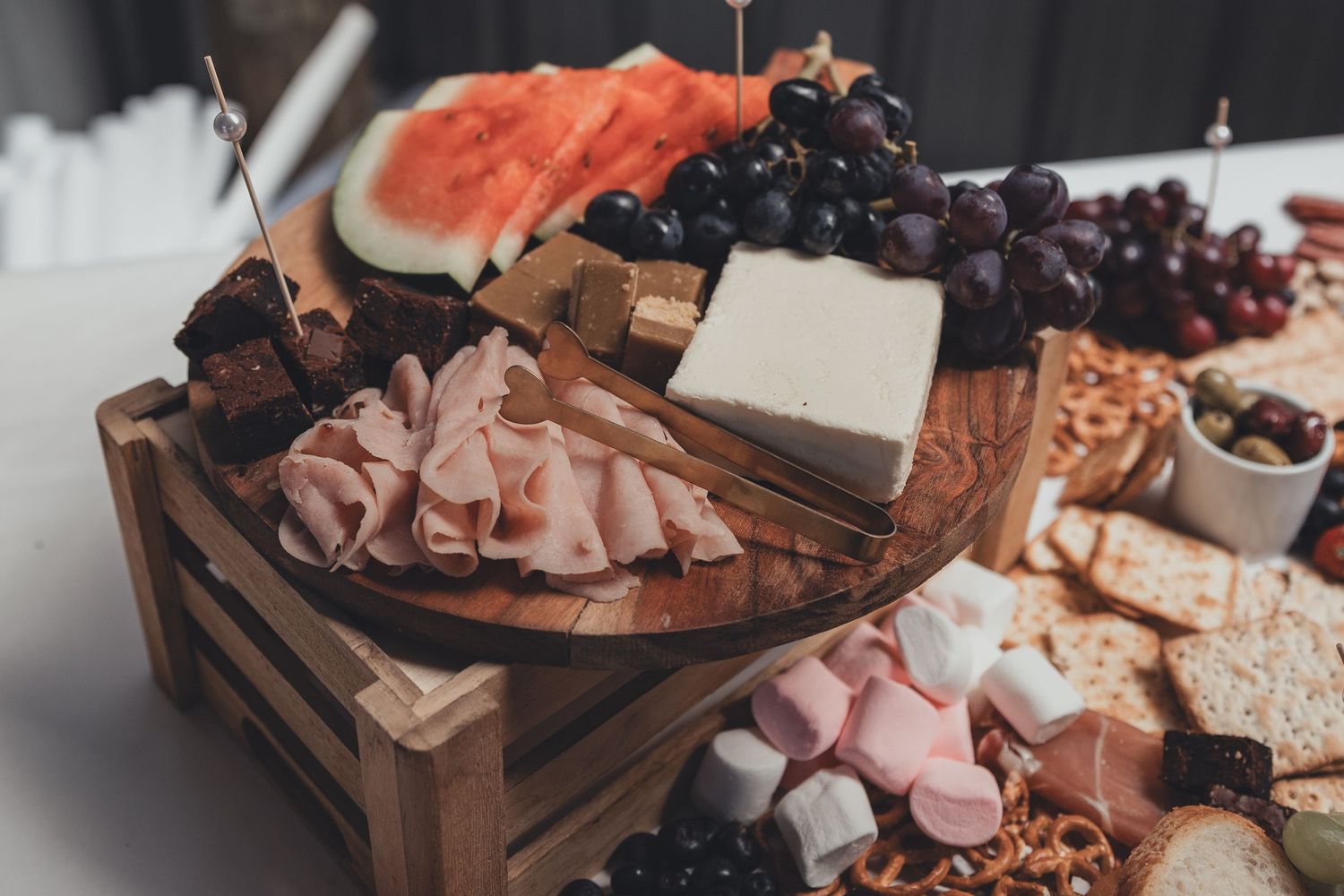 Elegant charcuterie board with cheese, ham, grapes, watermelon, marshmallows, and crackers on a wooden tray.
