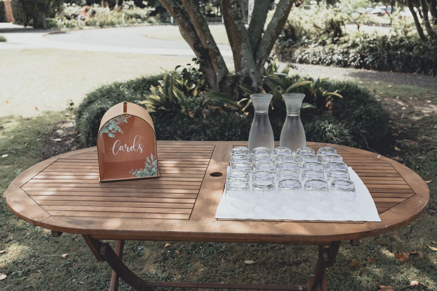 Outdoor wedding welcome table with cards sign, glass vases, and drinking glasses.