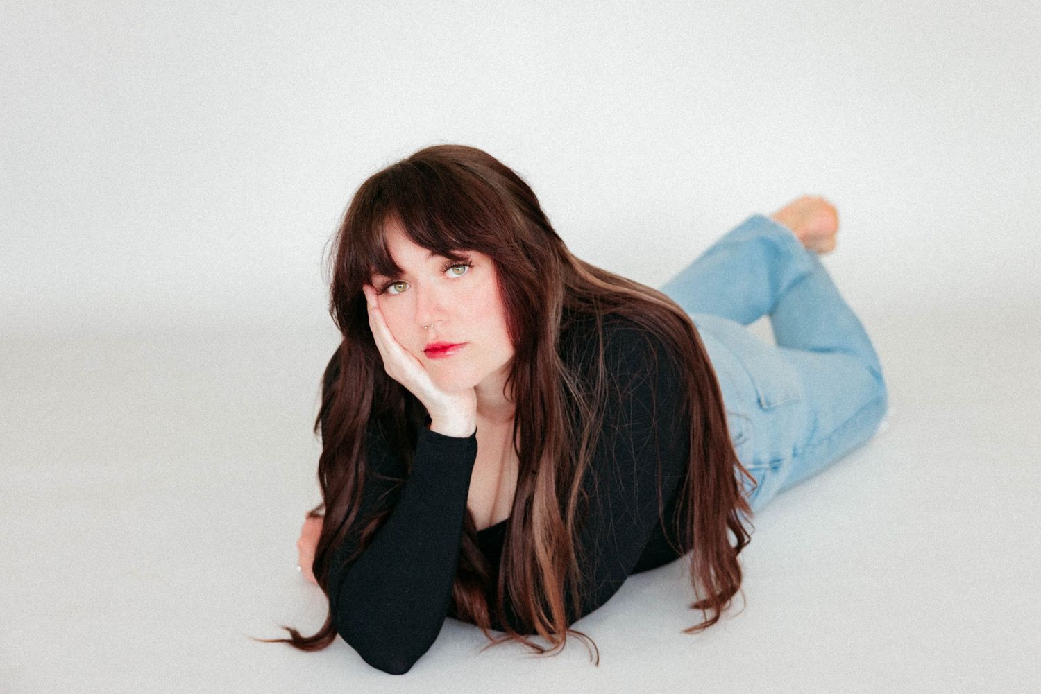 Woman with long brown hair lying on the floor posing in a bright white studio.