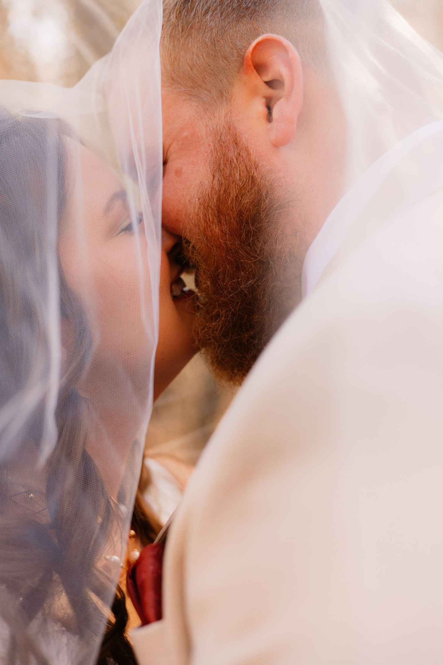 Romantic close-up of bride and groom sharing a kiss beneath a flowing white wedding veil.