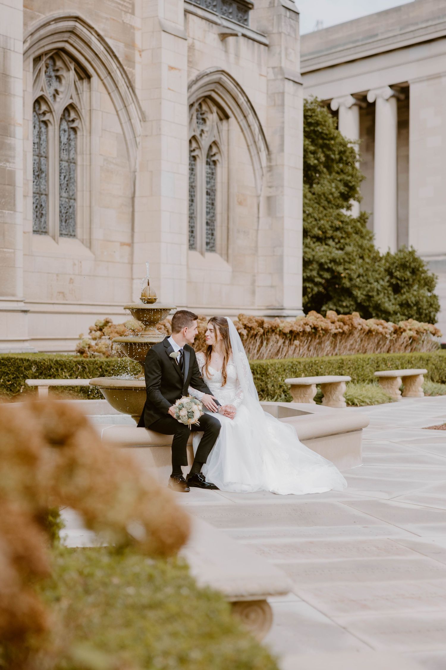Bride and groom sitting together outside a grand cathedral with lush gardens.