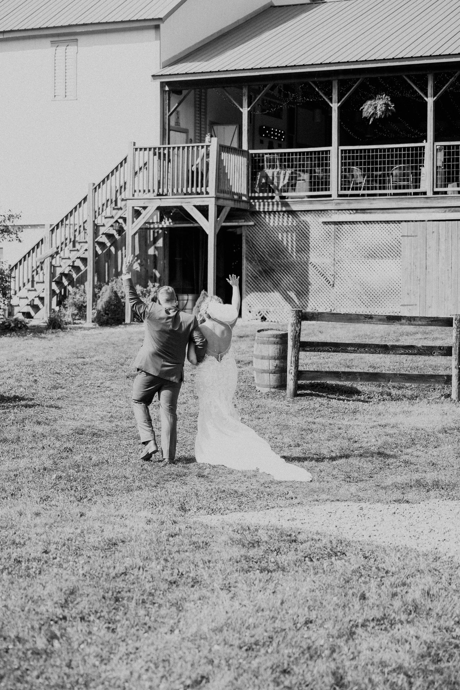 Black and white photo of bride and groom playfully dancing outside a rustic barn wedding venue.