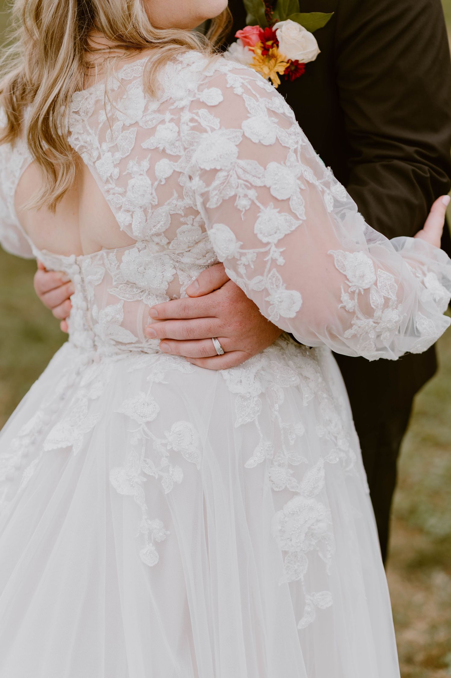 Close-up of bride's floral lace long-sleeve wedding gown with groom's hand on her waist.