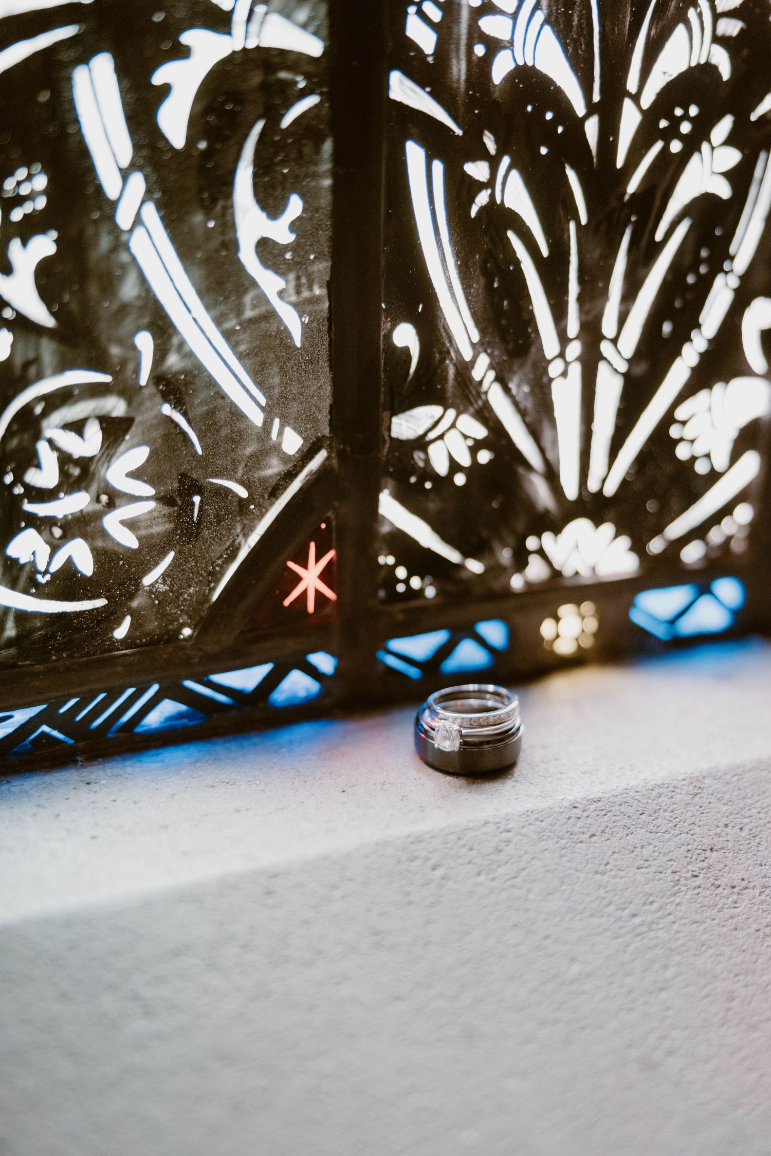 A wedding ring rests beside an ornate decorative lantern casting a red star pattern on a white surface.