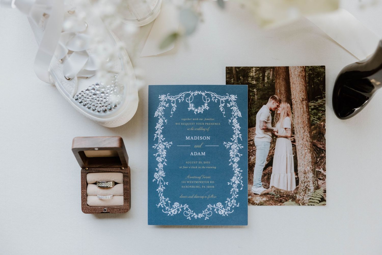 Blue floral wedding invitation suite with couple photo, ring box, and bridal shoes flat lay.
