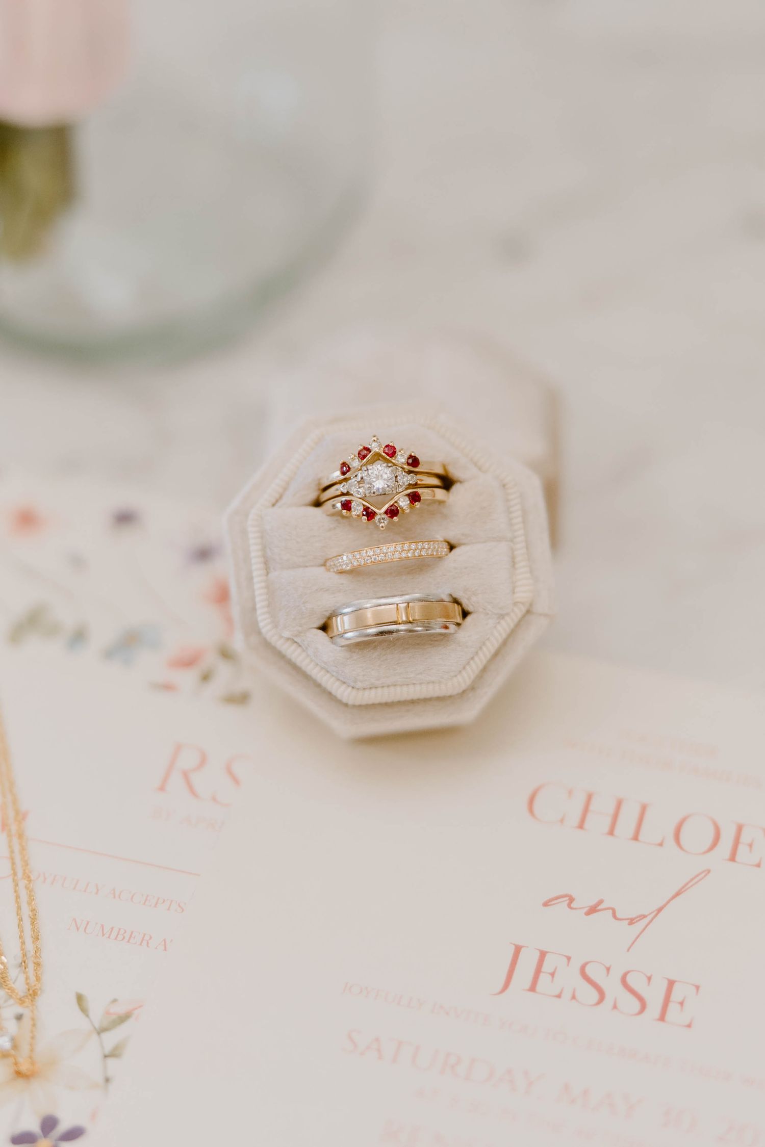 Wedding rings displayed in velvet box beside Chloe and Jesse wedding invitation.