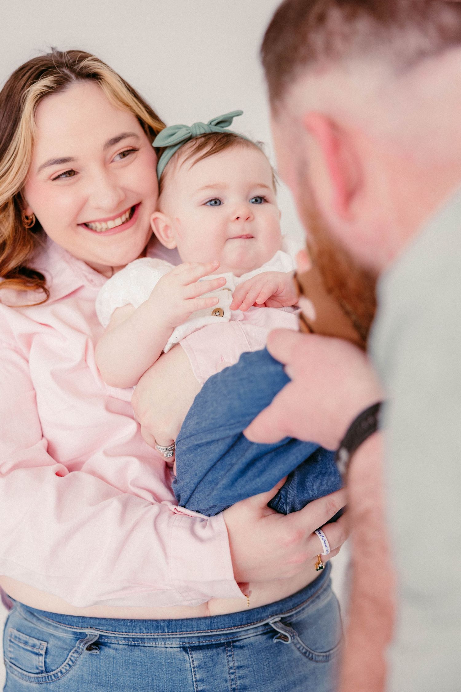 Smiling mother holding baby girl with father leaning in for a family portrait.
