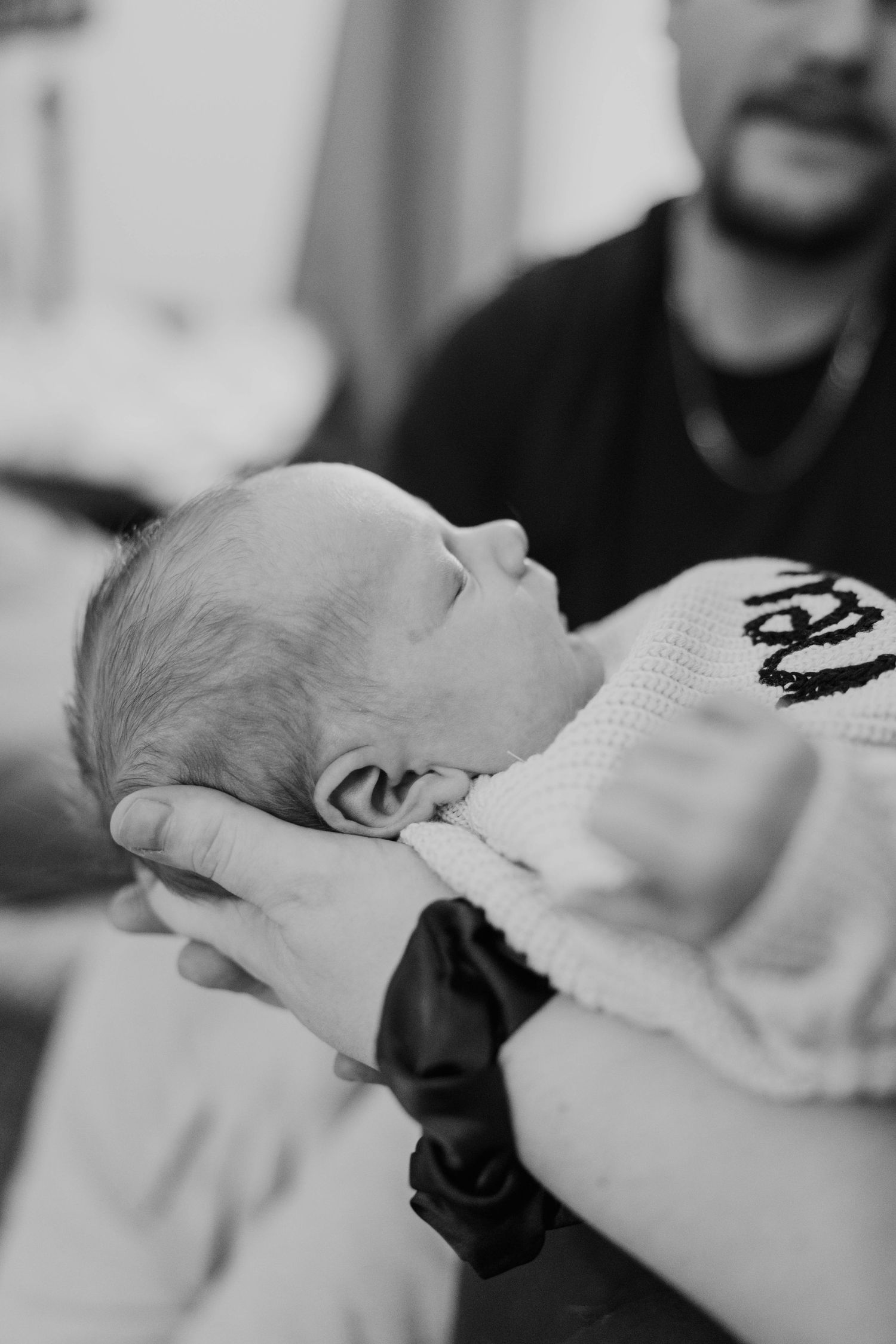 Black and white close-up of a newborn baby being cradled in a fathers hands.