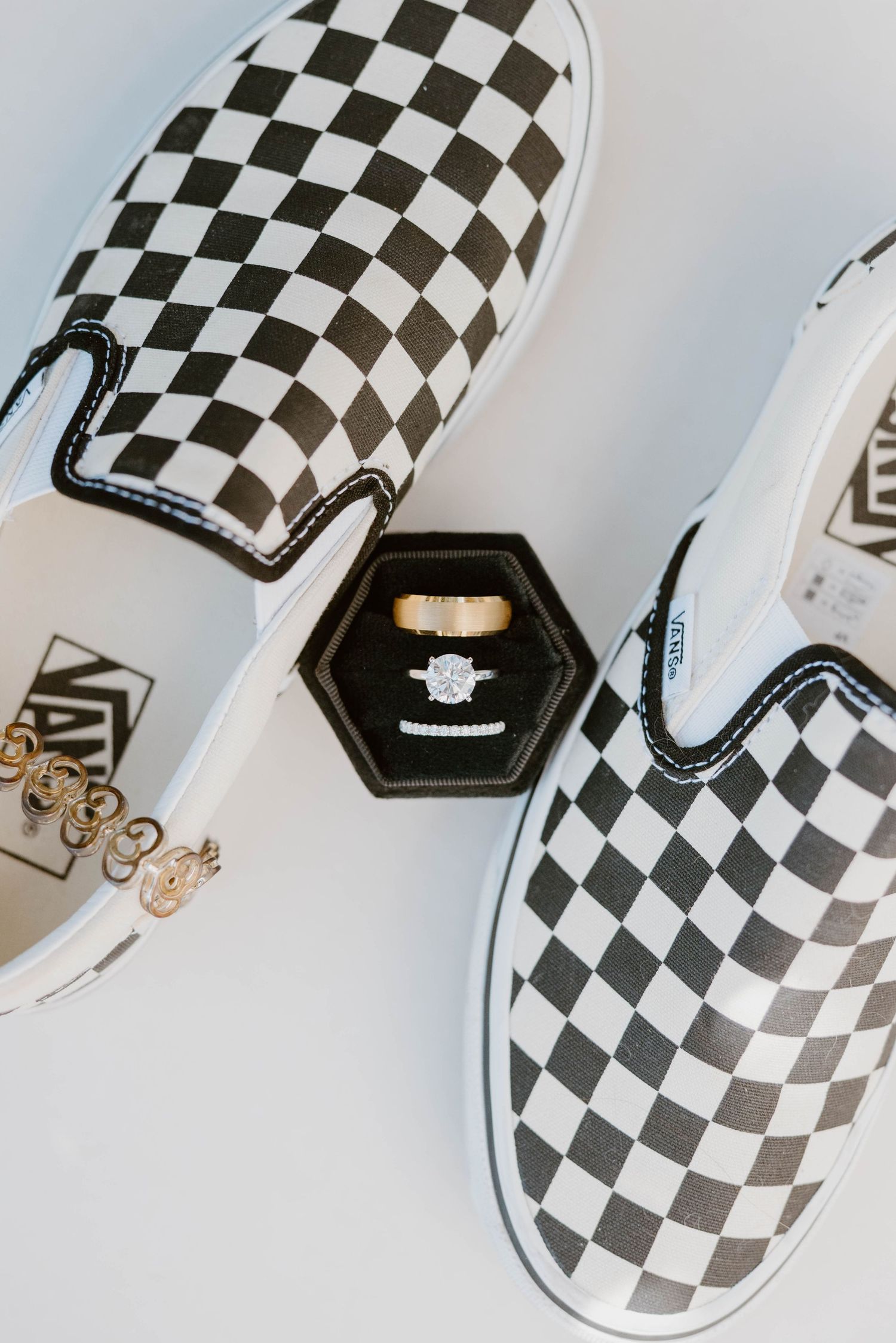 Black and white checkered Vans slip-on sneakers with wedding rings displayed in hexagon ring box.