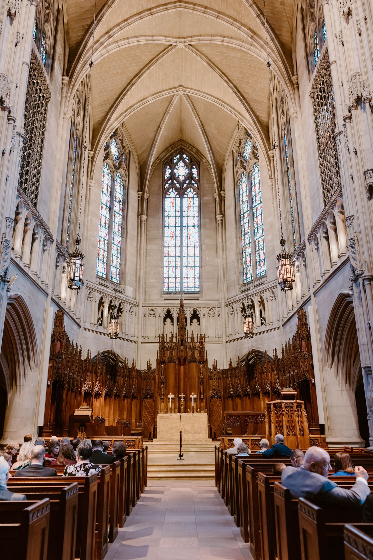 Guests seated in wooden pews inside a stunning Gothic cathedral with soaring arched ceilings and stained glass windows.