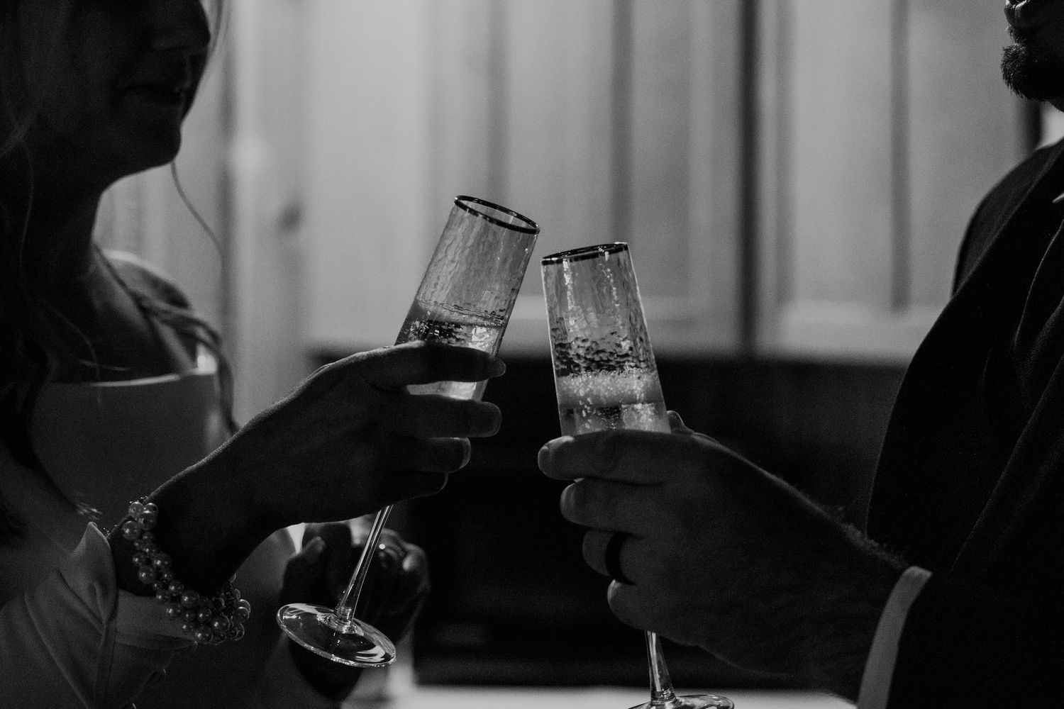 Black and white photo of a bride and groom toasting with champagne flutes to celebrate their wedding day.