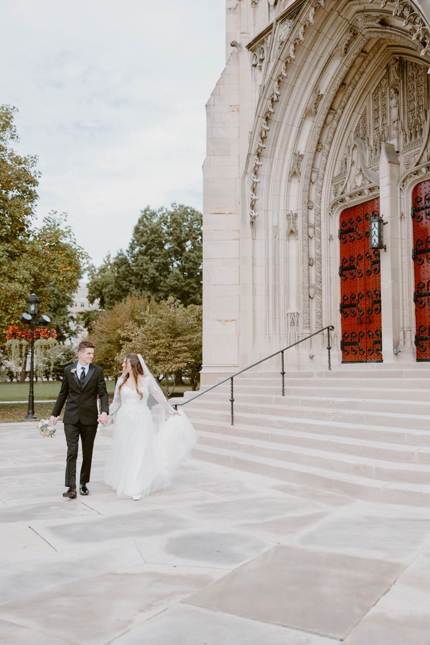Bride and groom holding hands walking down steps of an ornate Gothic cathedral on their wedding day.