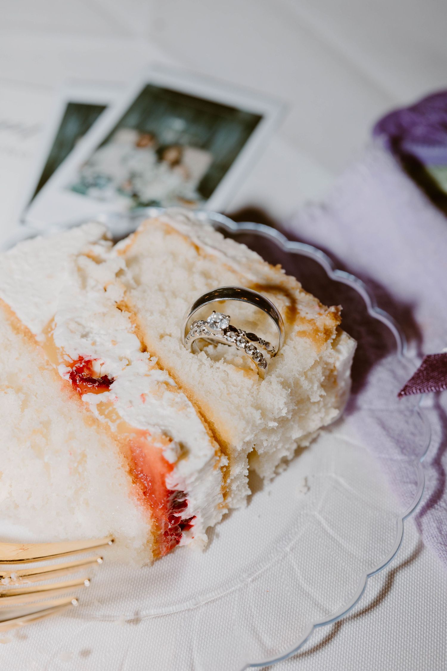 Wedding rings resting on a slice of white cake with strawberry filling on a decorative plate.