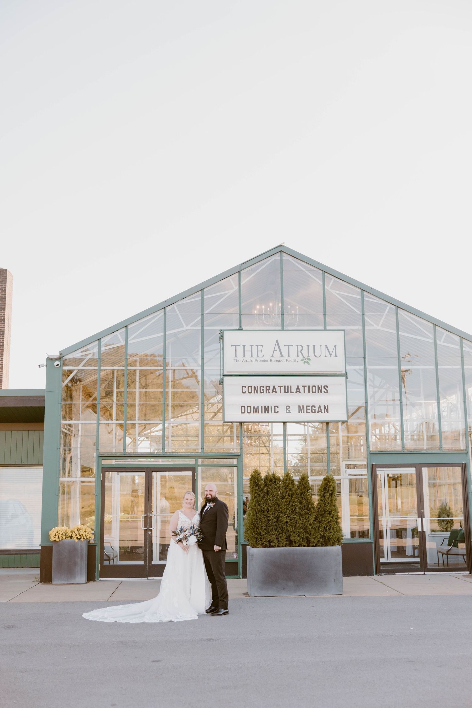 Bride and groom pose outside The Atrium venue displaying a congratulations sign at the Atrium in Butler, Pennsylvania.