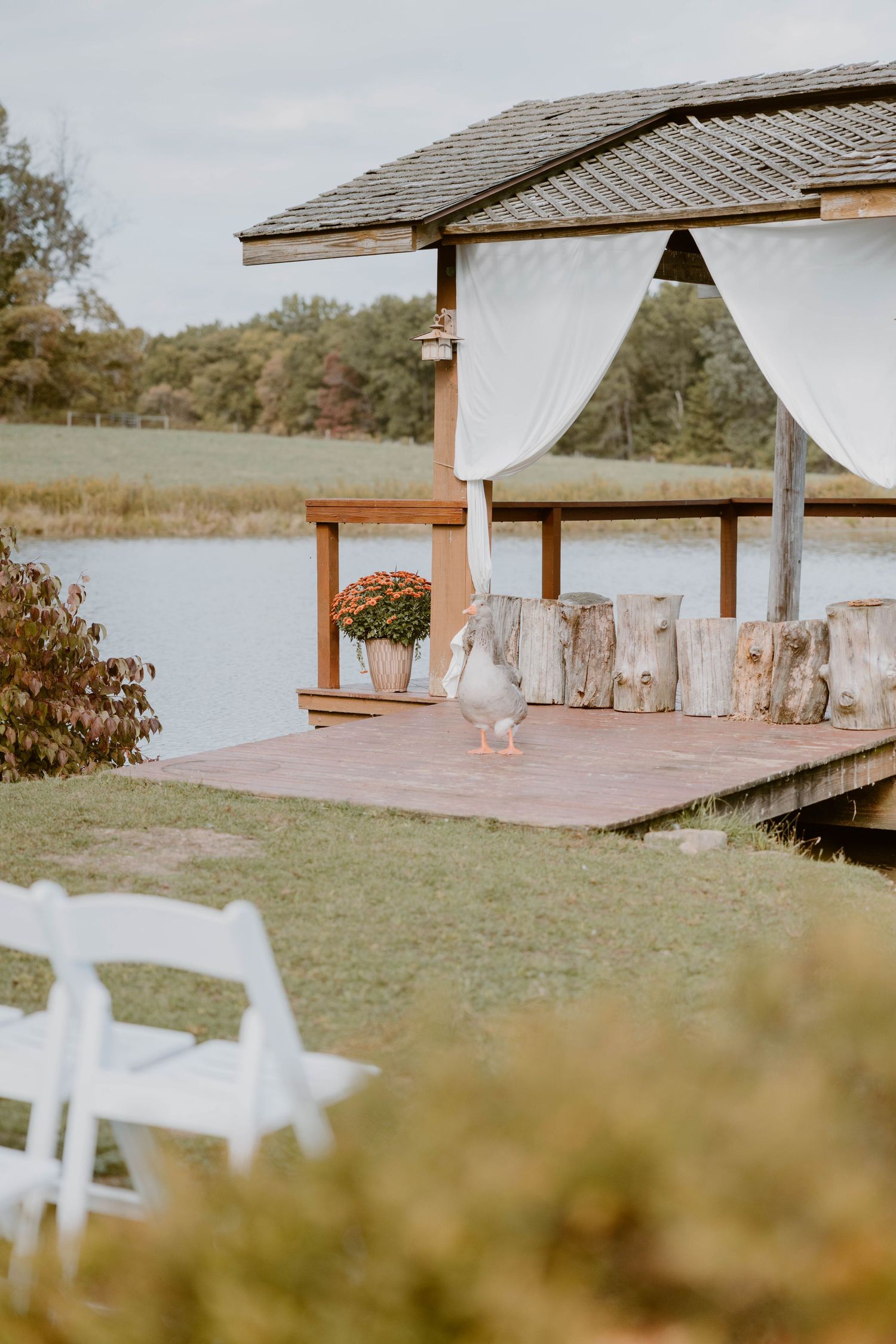 Elegant lakeside wedding ceremony gazebo with white draping curtains and floral decorations.