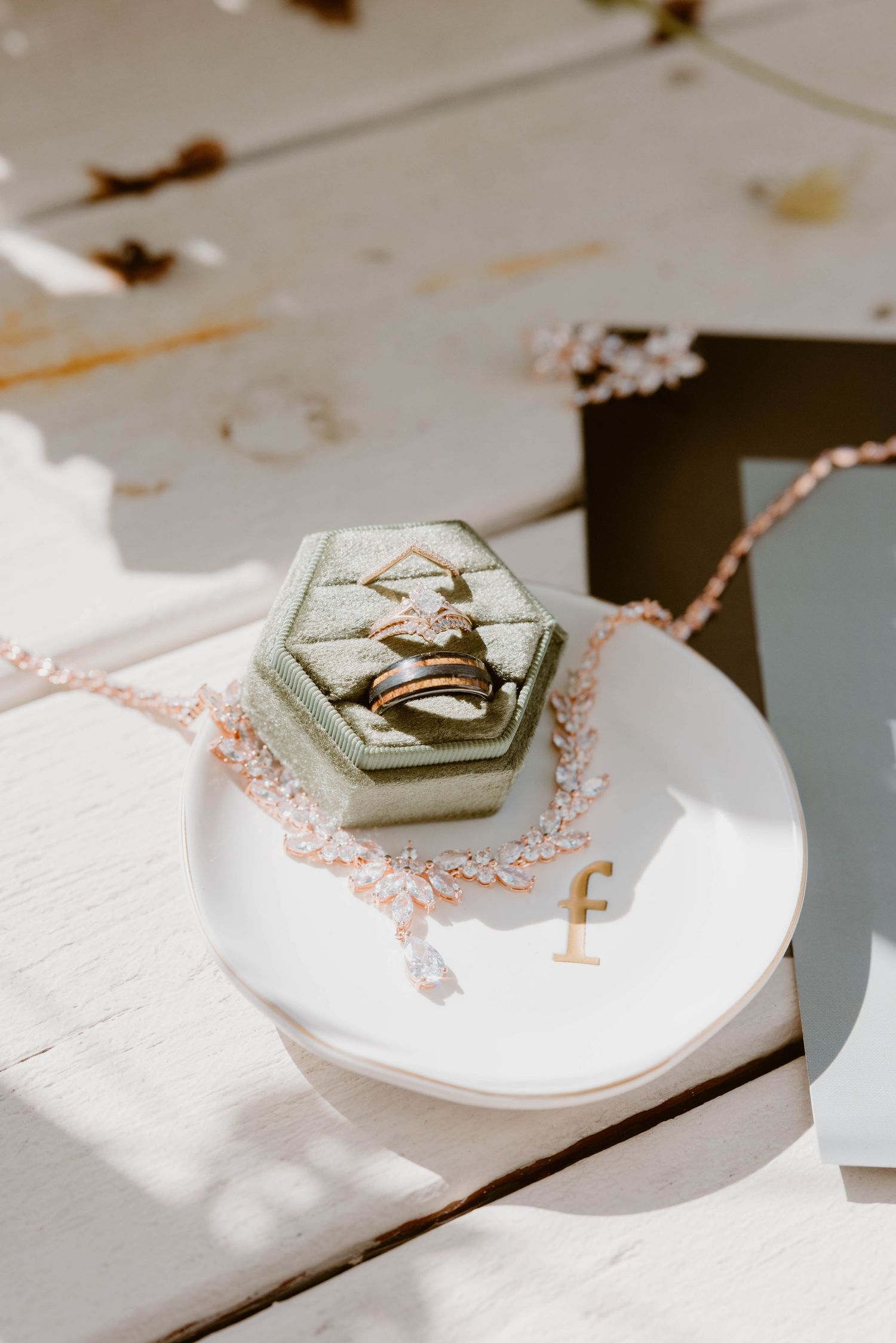 Gold wedding rings and diamond engagement ring displayed in a sage green velvet hexagon ring box on a white dish.