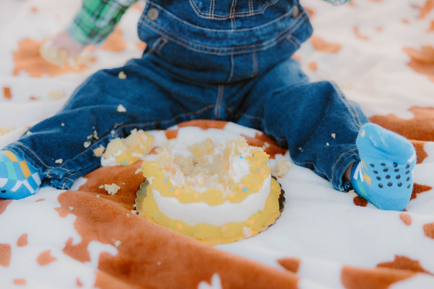 Close-up of a baby smashing a white frosted yellow first birthday cake on a cowhide blanket.