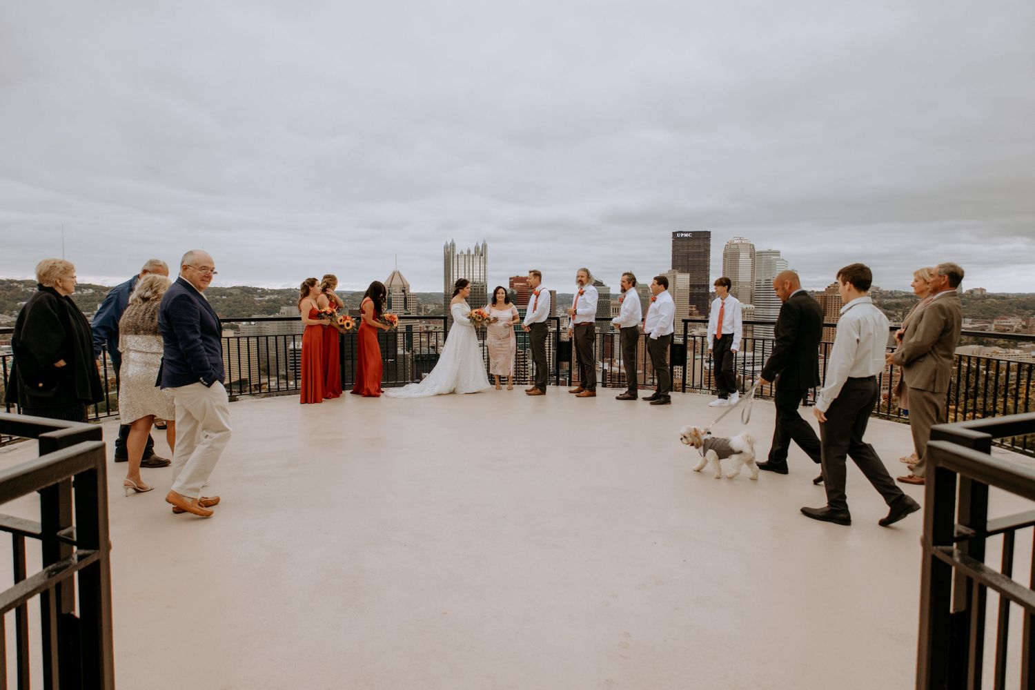 Rooftop wedding ceremony with city skyline backdrop, bridal party in red dresses and guests gathered around couple.