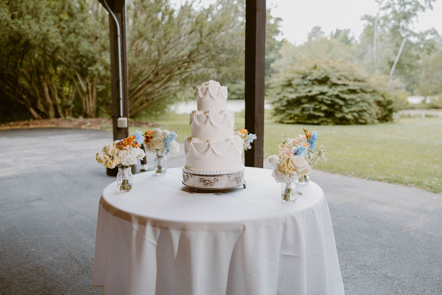 Elegant three-tier white wedding cake displayed on a table by a garden window.