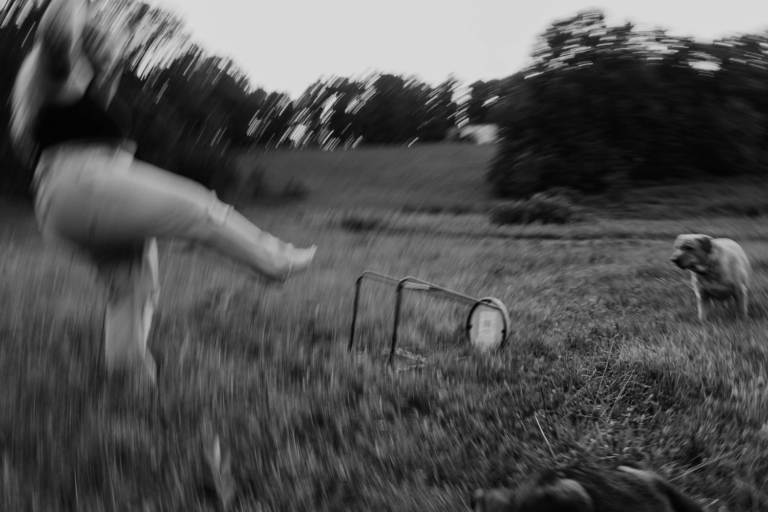 Black and white photo of person running in a field with a dog near a metal garden gate.