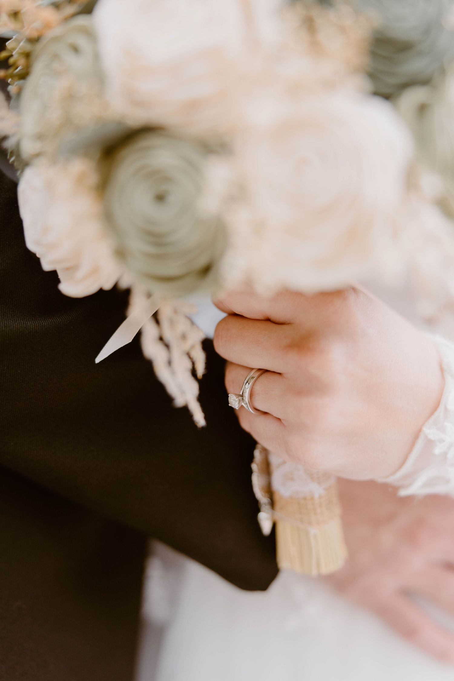 Close-up of a bride's hand with wedding ring holding a white floral bouquet.