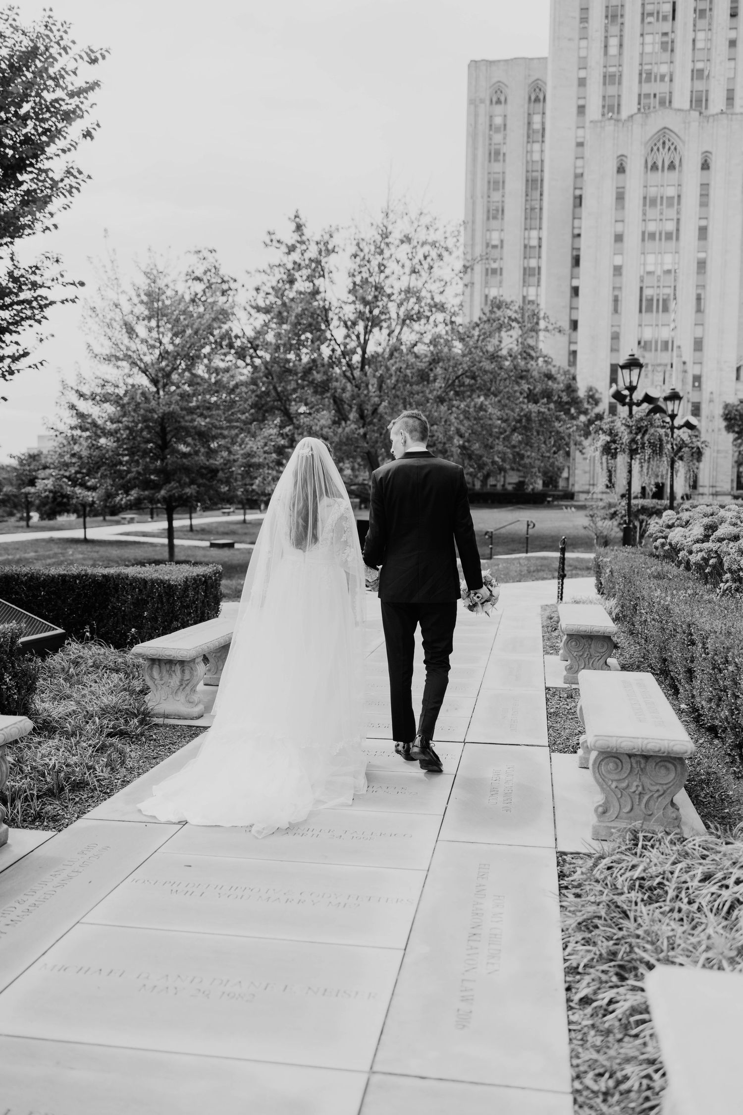 Black and white photo of bride and groom walking hand in hand near a cathedral.