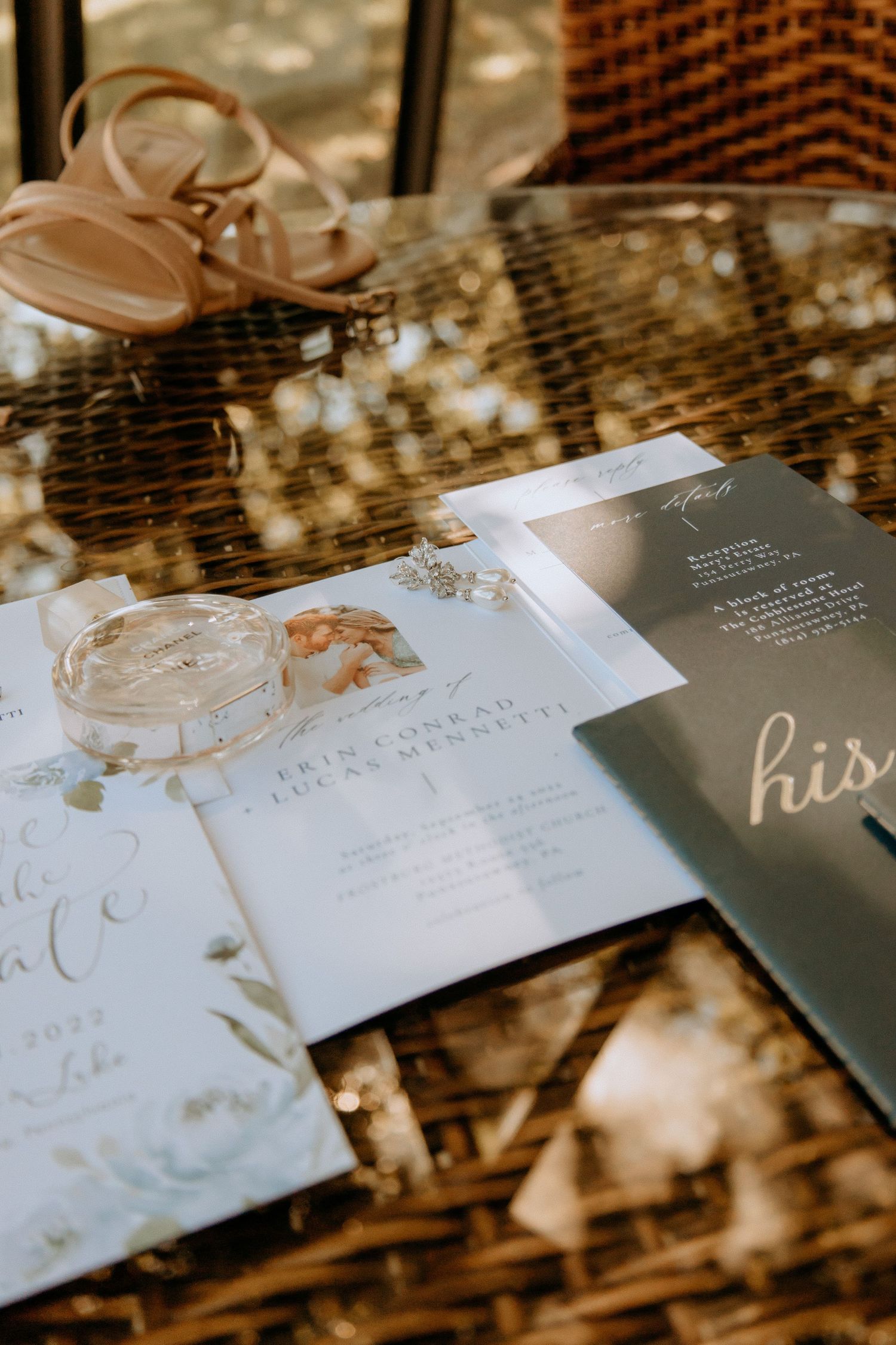 Elegant wedding stationery, rings, and bridal heels arranged on a wicker table for a styled flat lay.