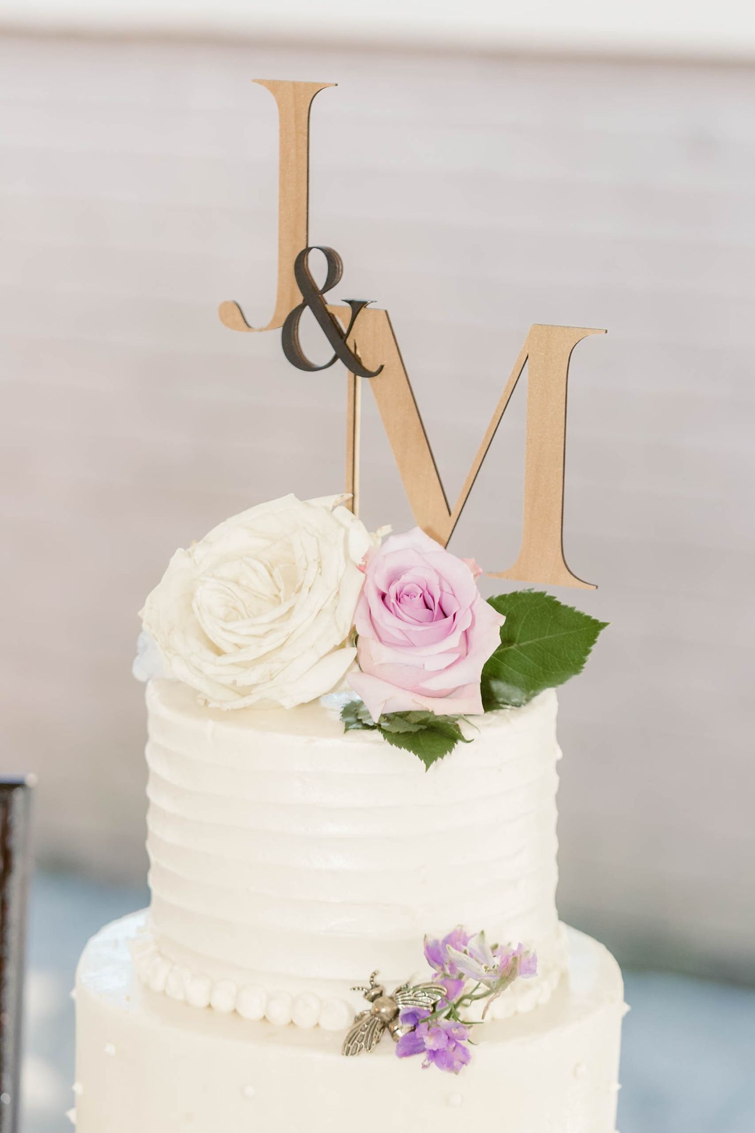 White wedding cake topped with gold J&M monogram and fresh roses.