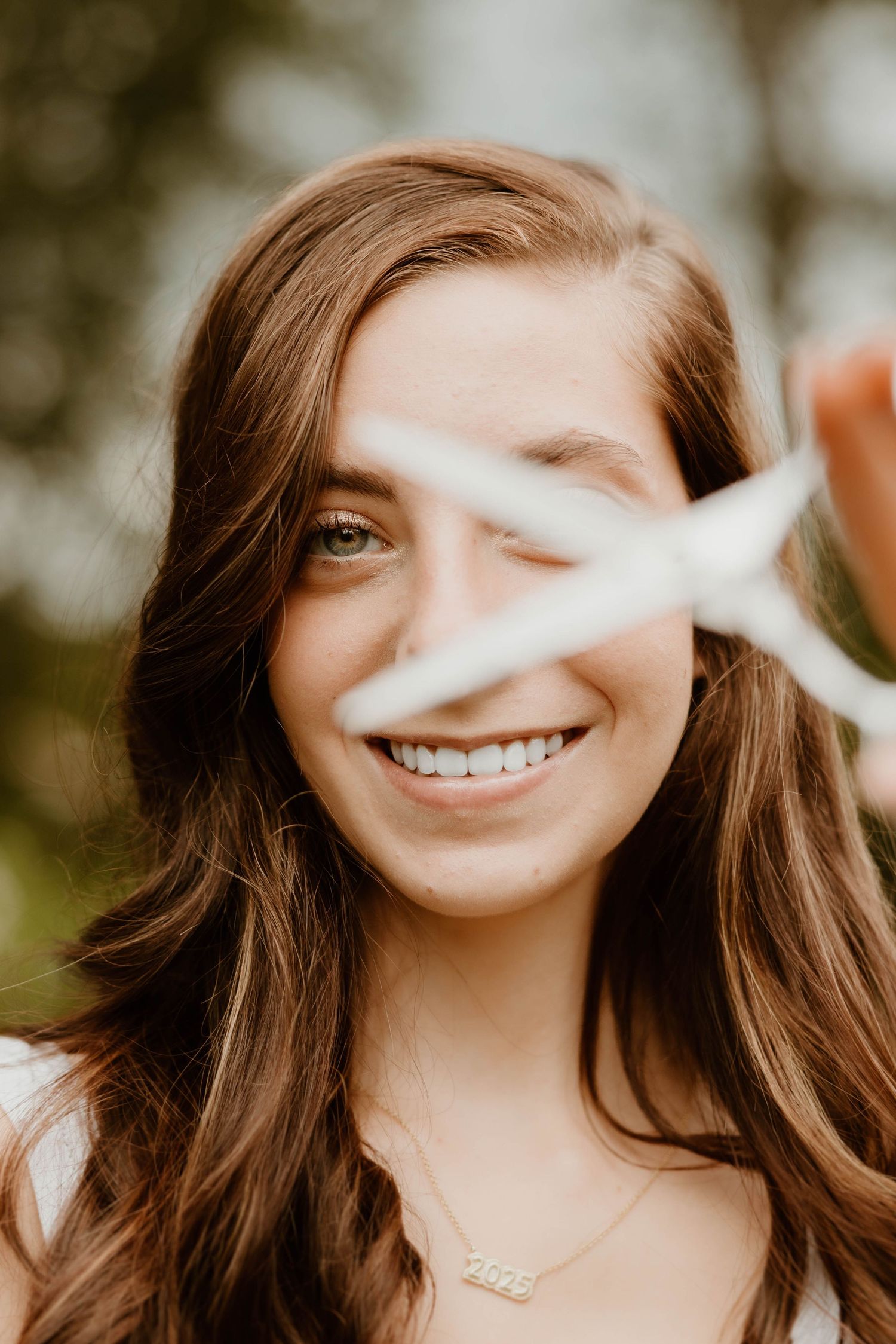 Smiling young woman with brown hair holds a white star prop in a playful outdoor portrait.