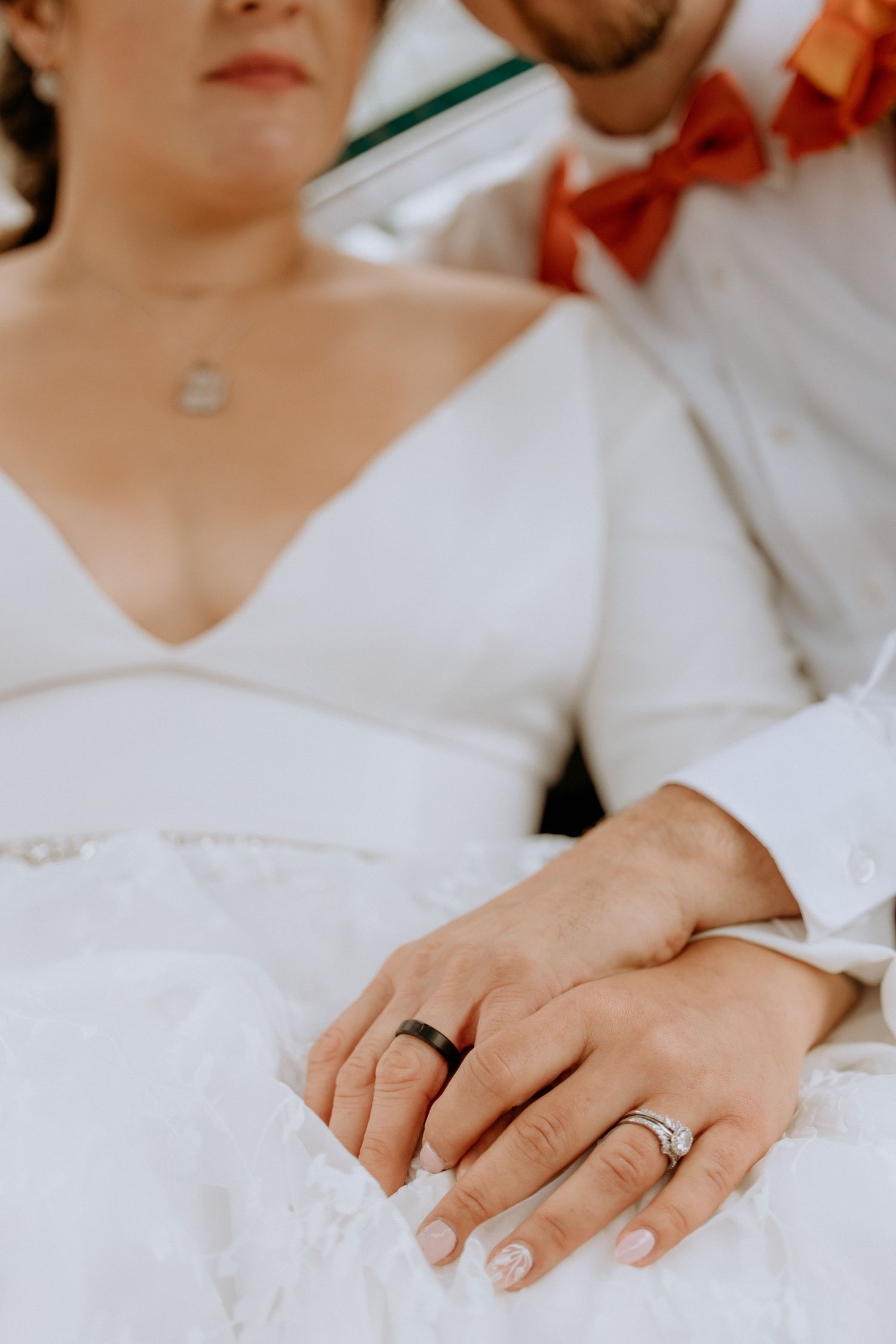 Close-up of newlyweds holding hands, showing wedding bands, bride wearing a diamond ring.