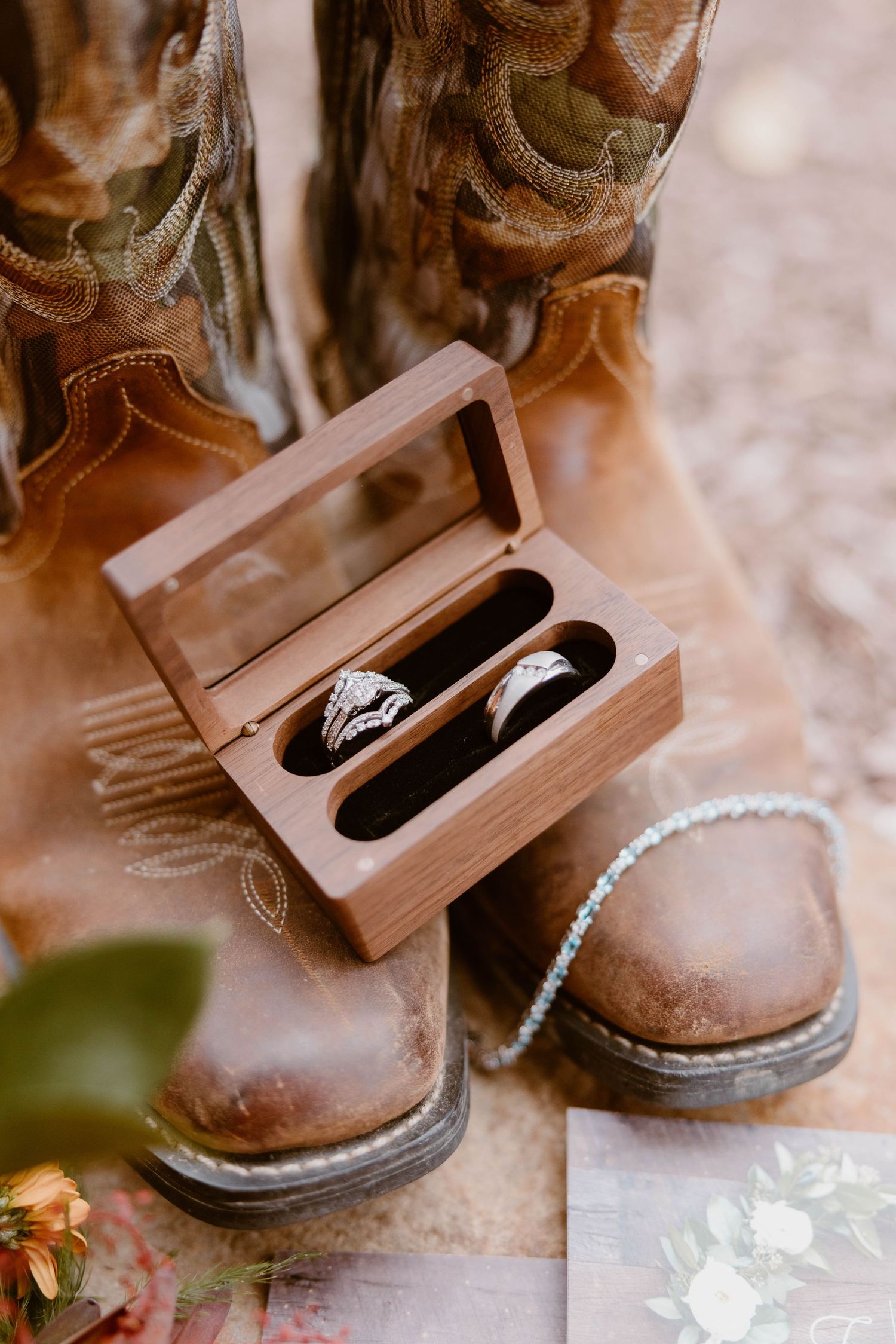 Wedding rings displayed in a wooden box atop rustic cowboy boots for a country-themed ceremony.