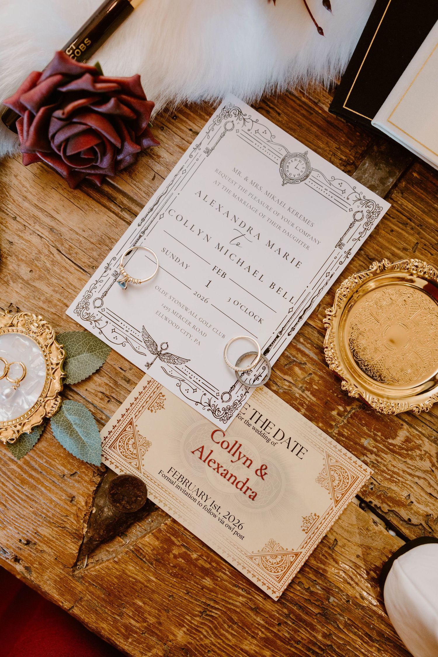 Wedding invitation suite for Collyn and Alexandra displayed on rustic wood with gold accents and a burgundy rose.
