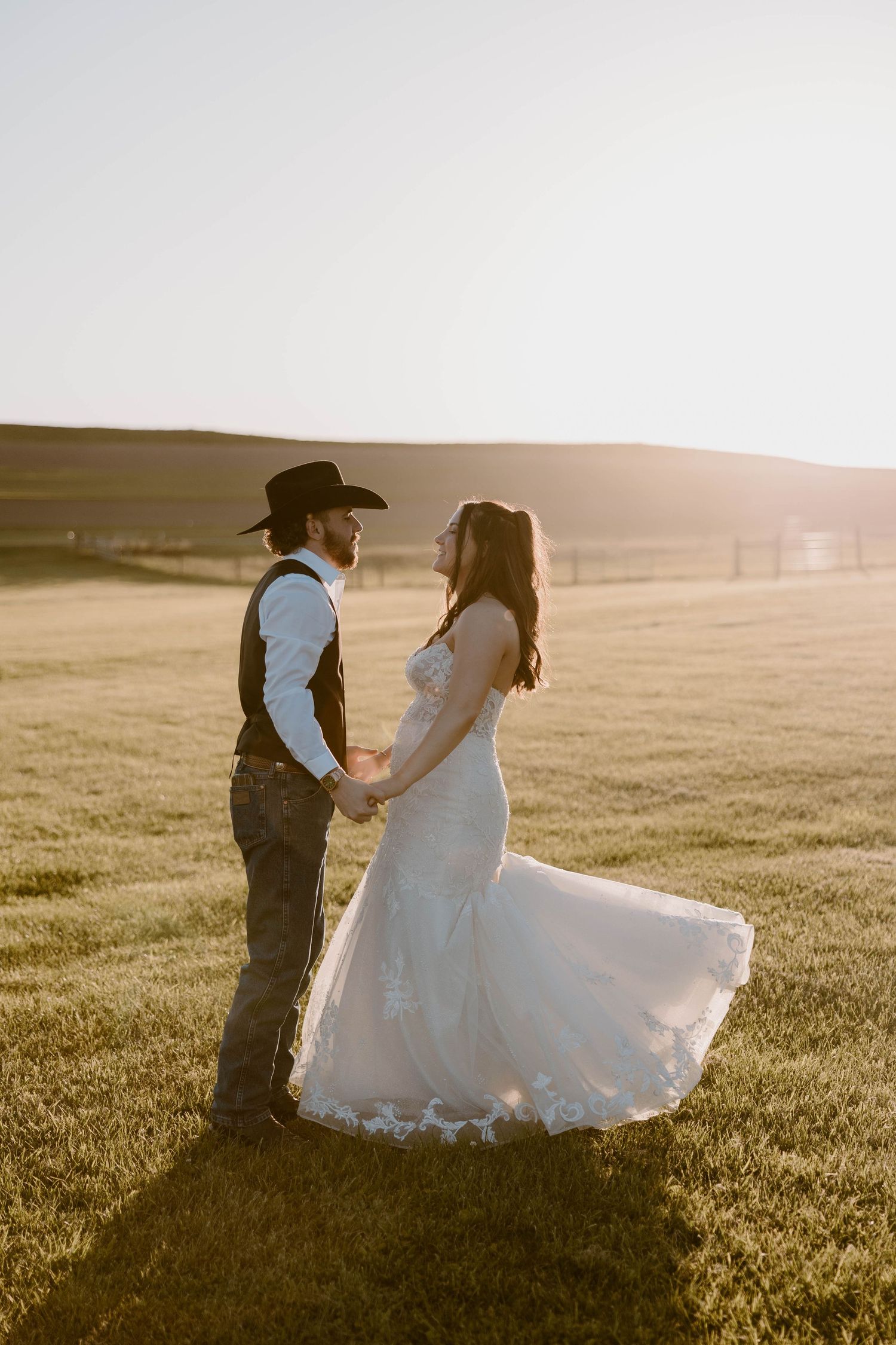 Bride and groom holding hands at golden hour in an open field at sunset.
