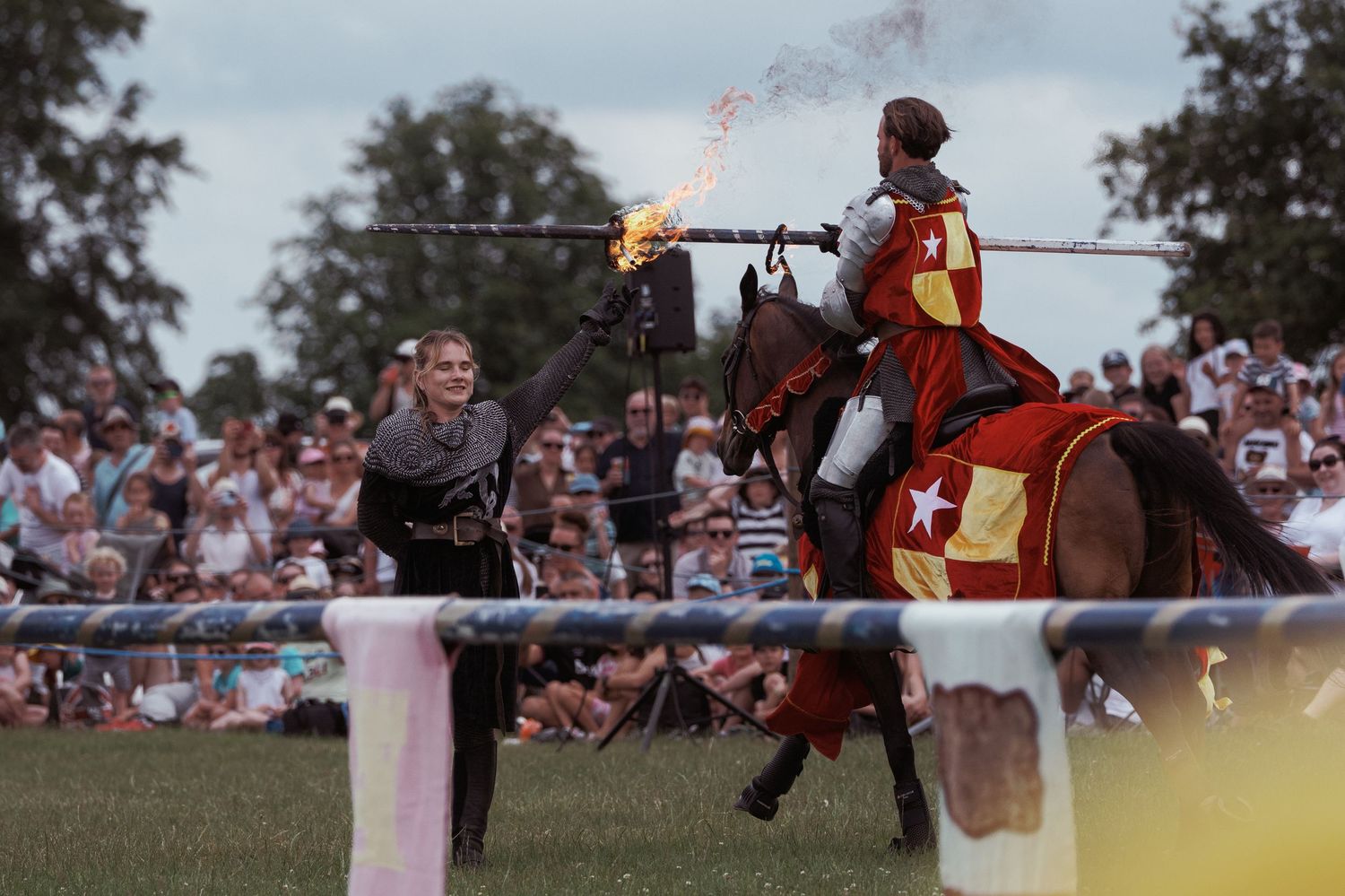 Medieval jousting knight on horseback with flaming lance at Renaissance faire with crowd of spectators.