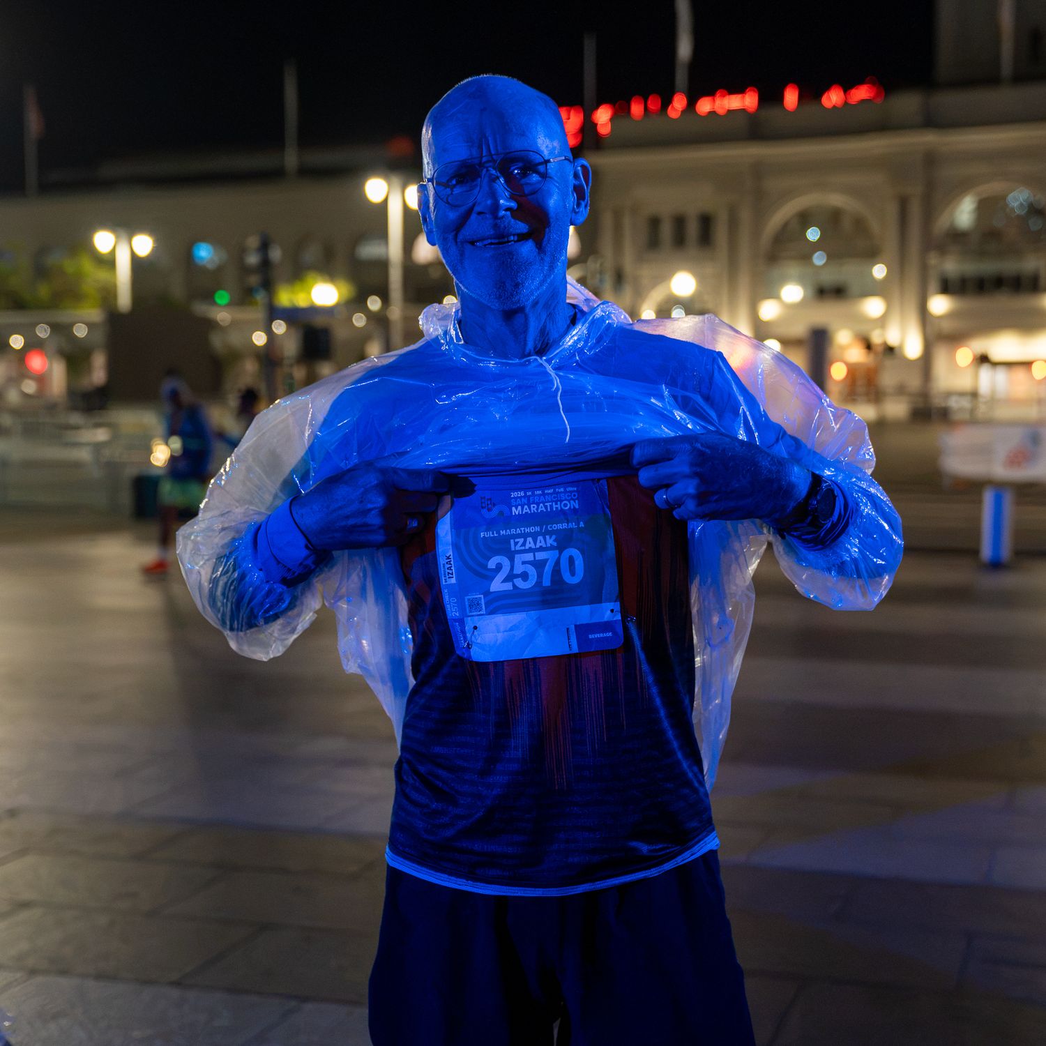 A blue-lit marathon runner wearing bib number 2570 poses at night, showing off his race number at an urban event.