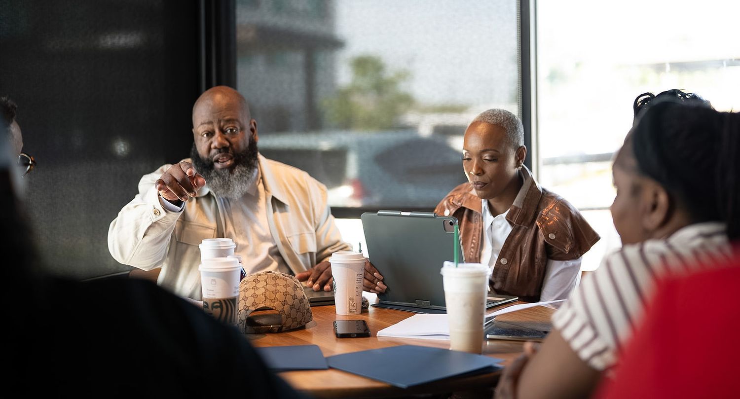 Group of people having a business meeting at a restaurant table with drinks and laptops.