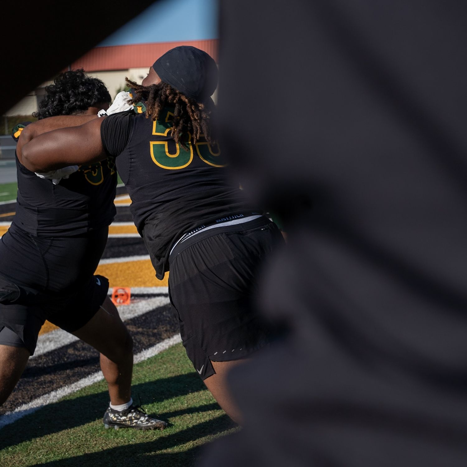 Two football players in black uniforms practice blocking drills on a field during training.