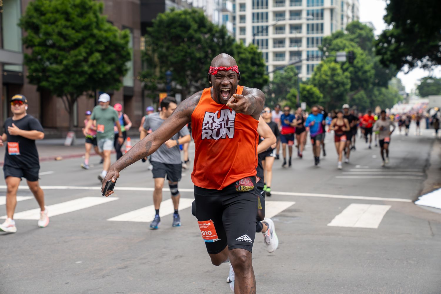 Energetic runner in orange Run shirt smiling during a city road race with other participants in background.