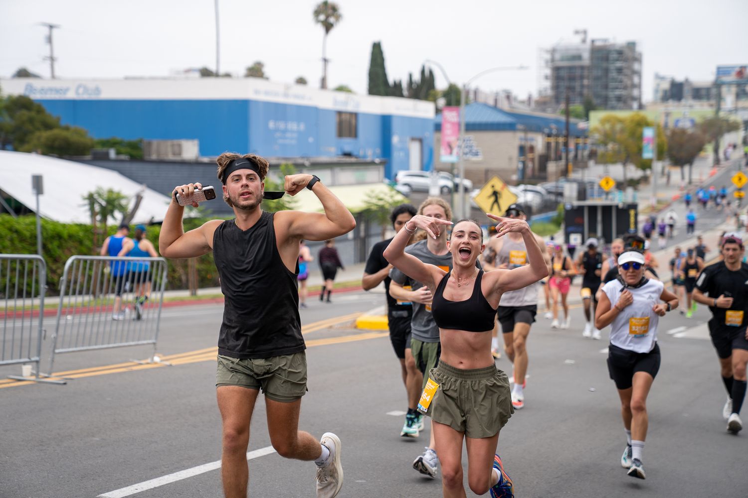 Runners celebrate during a street race in Los Angeles, with a man and woman cheering near the finish line on a sunny day.