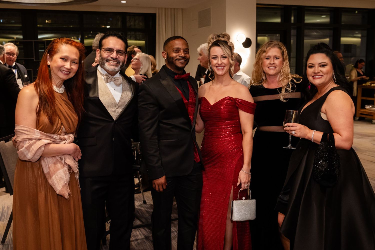 Elegantly dressed group of six posing together at a formal gala event in evening wear.