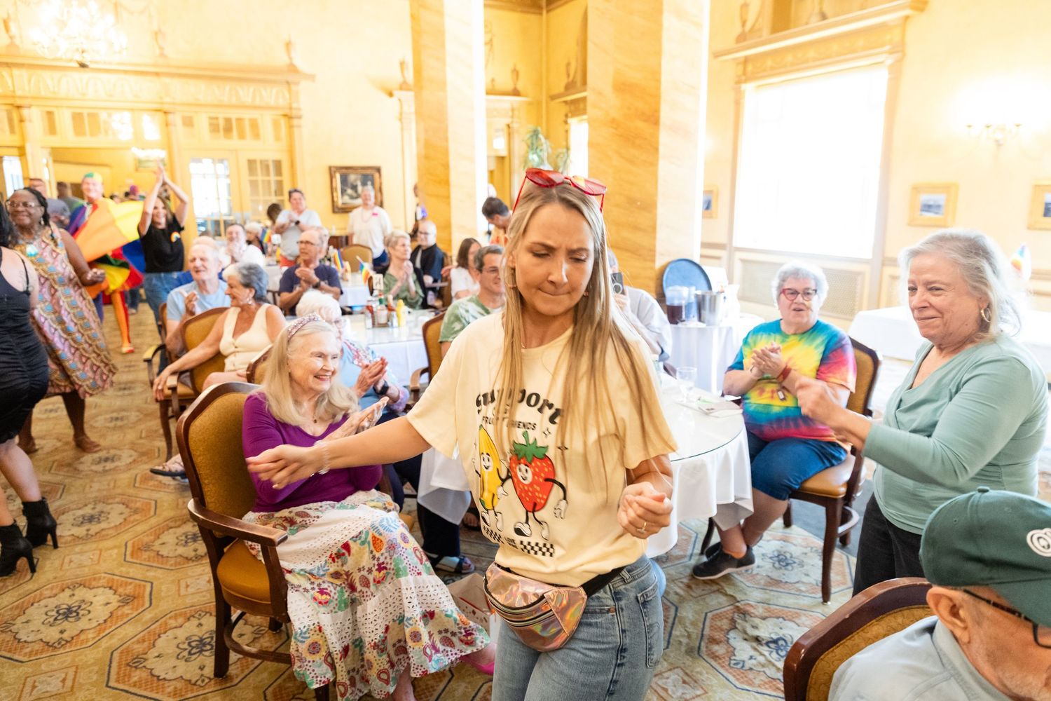 Young woman in casual outfit interacting with elderly guests at a lively community gathering in a grand hall.