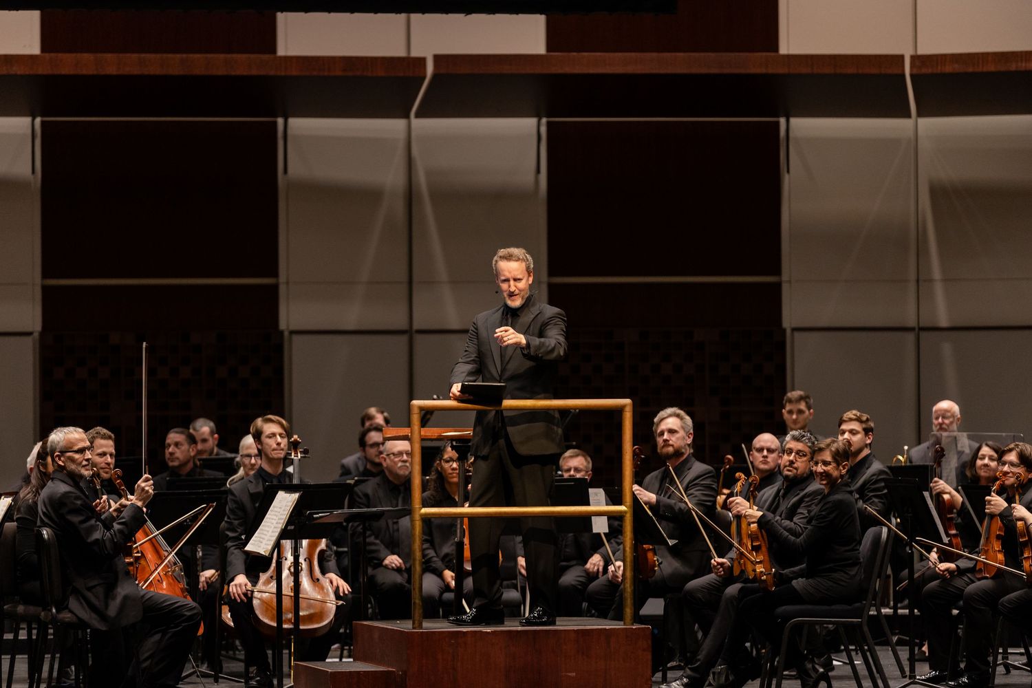 Dynamic conductor leading a large symphony orchestra during a live classical music performance on stage.