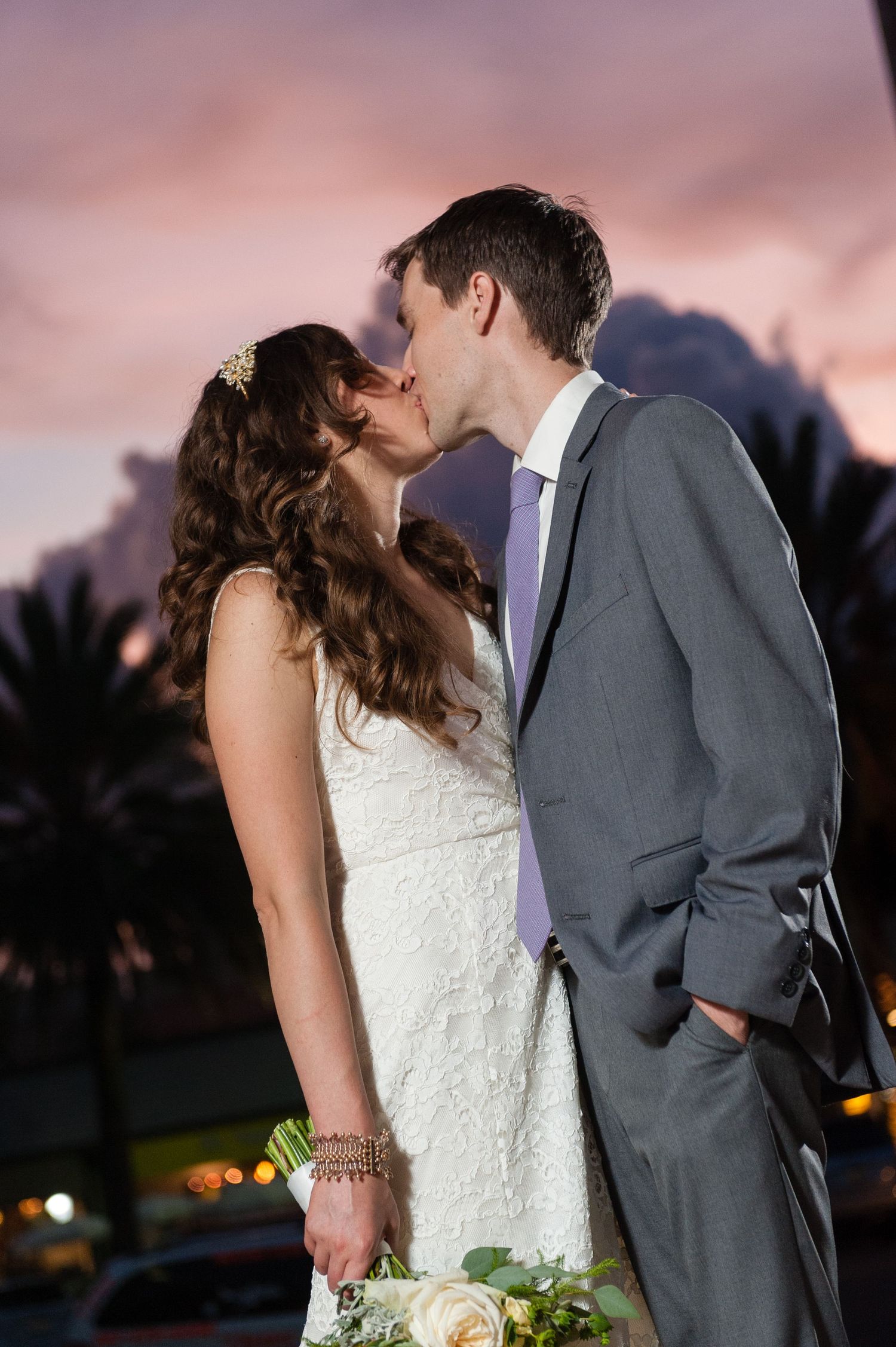 Bride and groom share a romantic kiss at sunset with colorful pink and purple sky backdrop in Museum of Fine Arts, St. Petersburg.