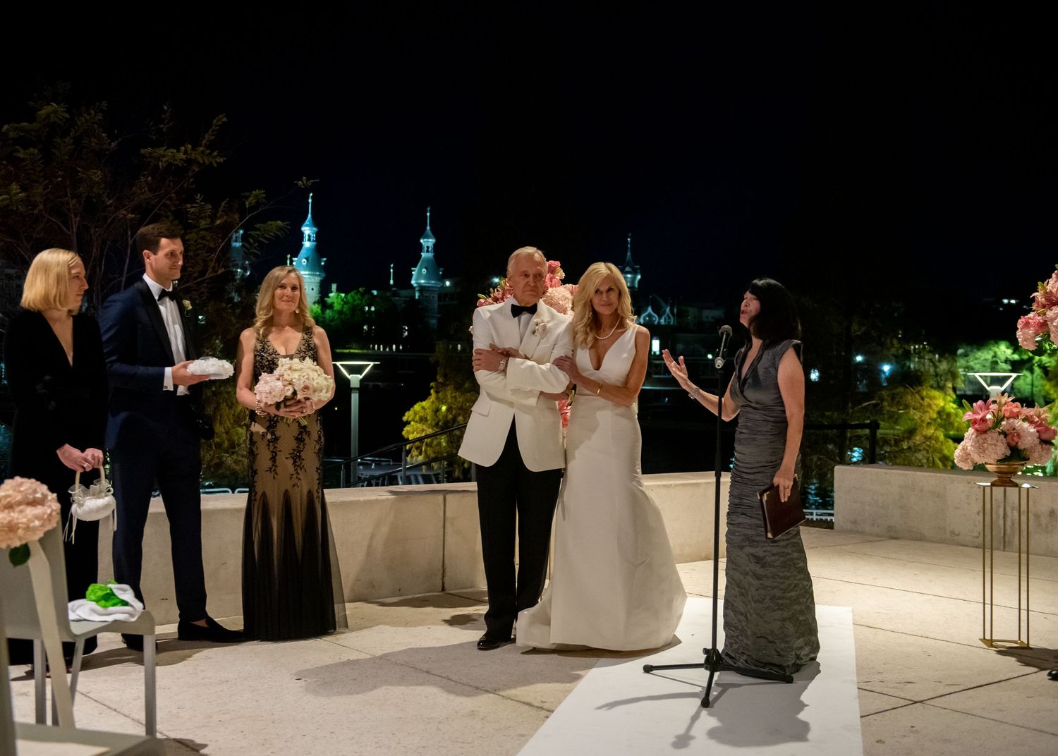 Wedding ceremony on outdoor terrace at night with bridal party and officiant before illuminated skyline in at Tampa museum of fine art.