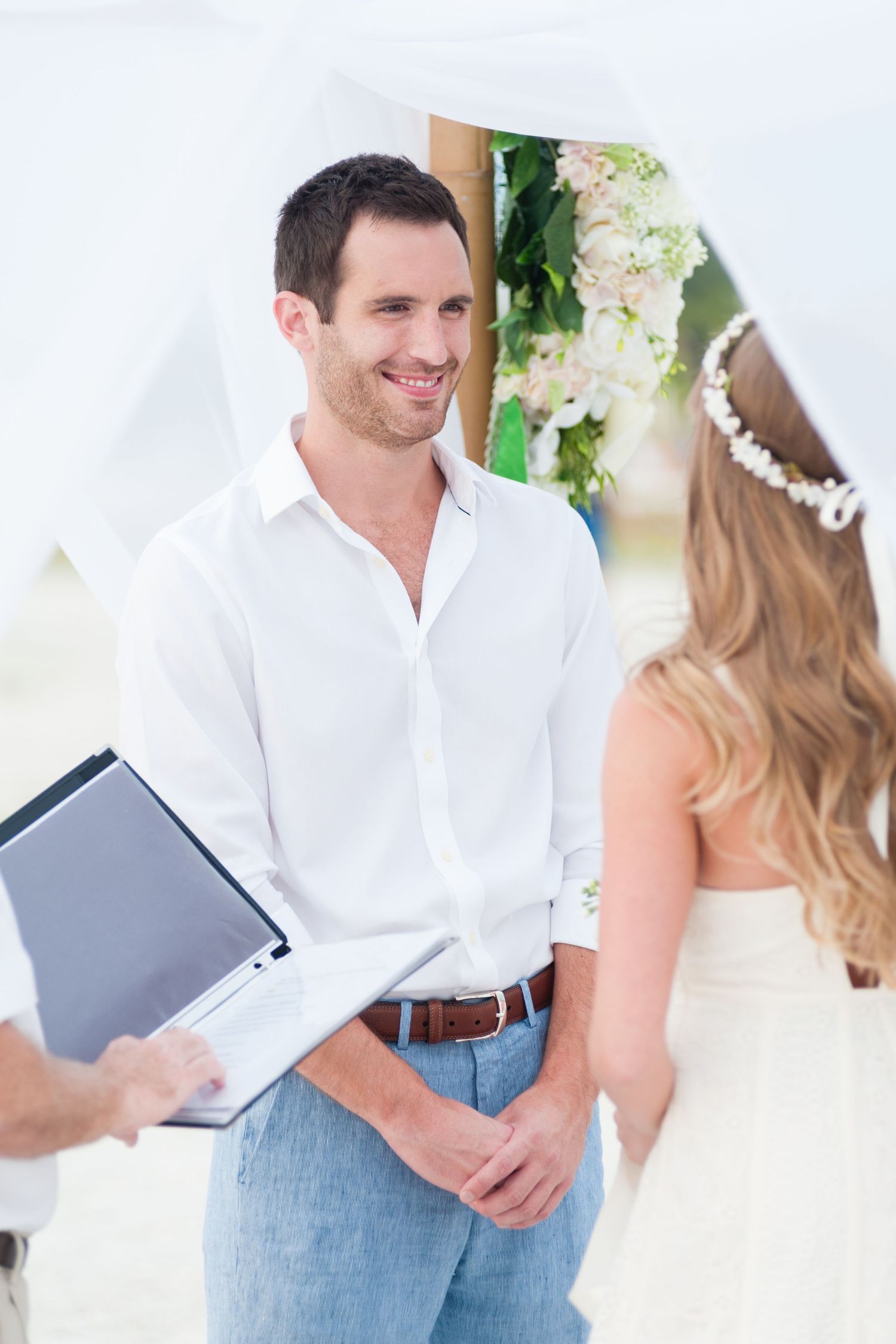Smiling groom in white shirt faces bride under floral arch at beach wedding on Treasure Island, Florida.