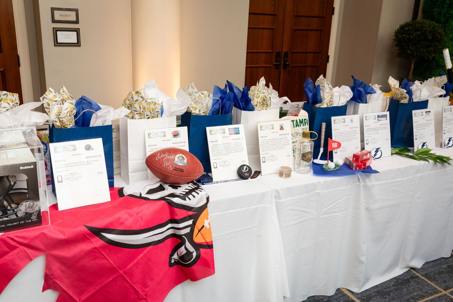 Silent auction table displaying sports memorabilia and gift bags at a charity fundraiser.
